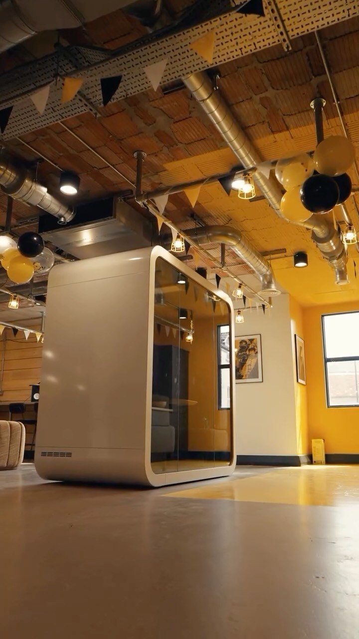 White soundproof office pod in a room with yellow walls and industrial ceiling.