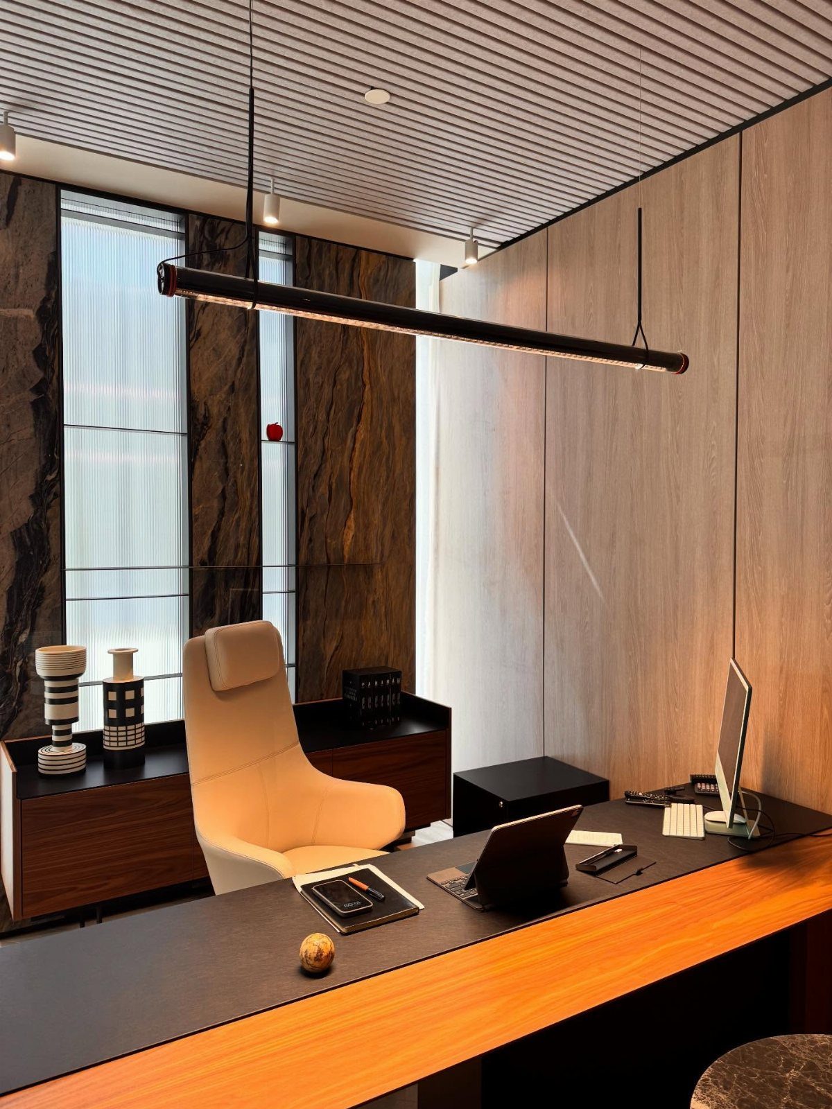 Long black linear pendant lamp hanging over a modern office desk and chair