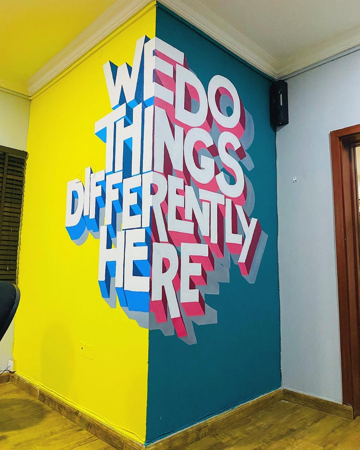 3D typographic wall mural saying We Do Things Differently Here on yellow and teal walls