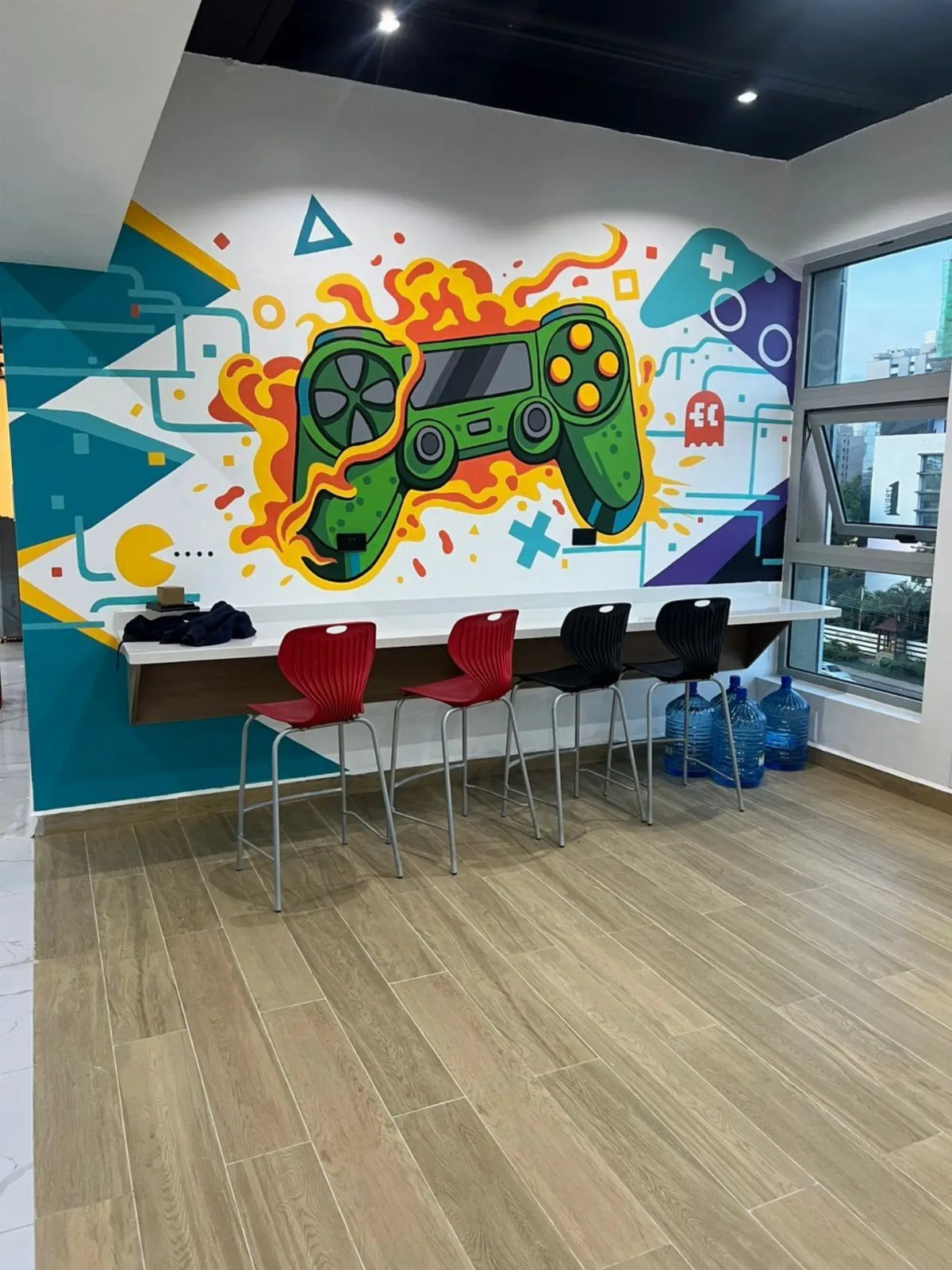 Colorful gaming controller wall mural above a long desk with four chairs.