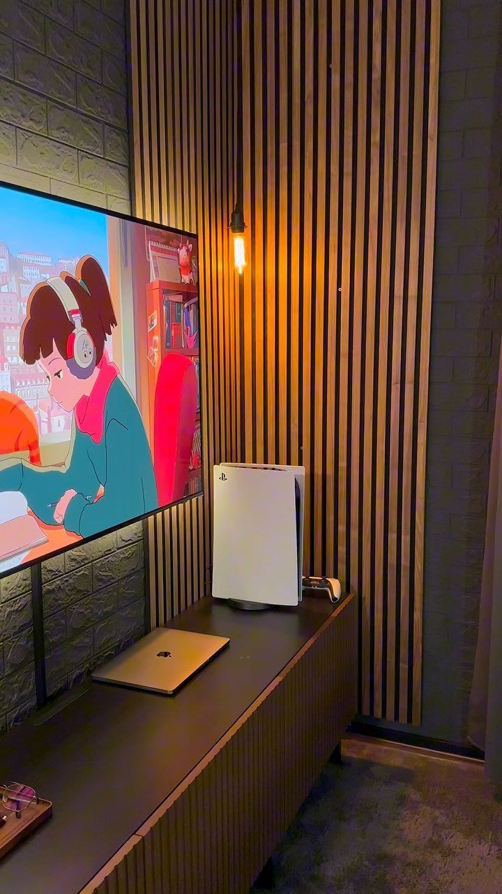 Large TV and gaming console on a wooden console against a slatted wall.