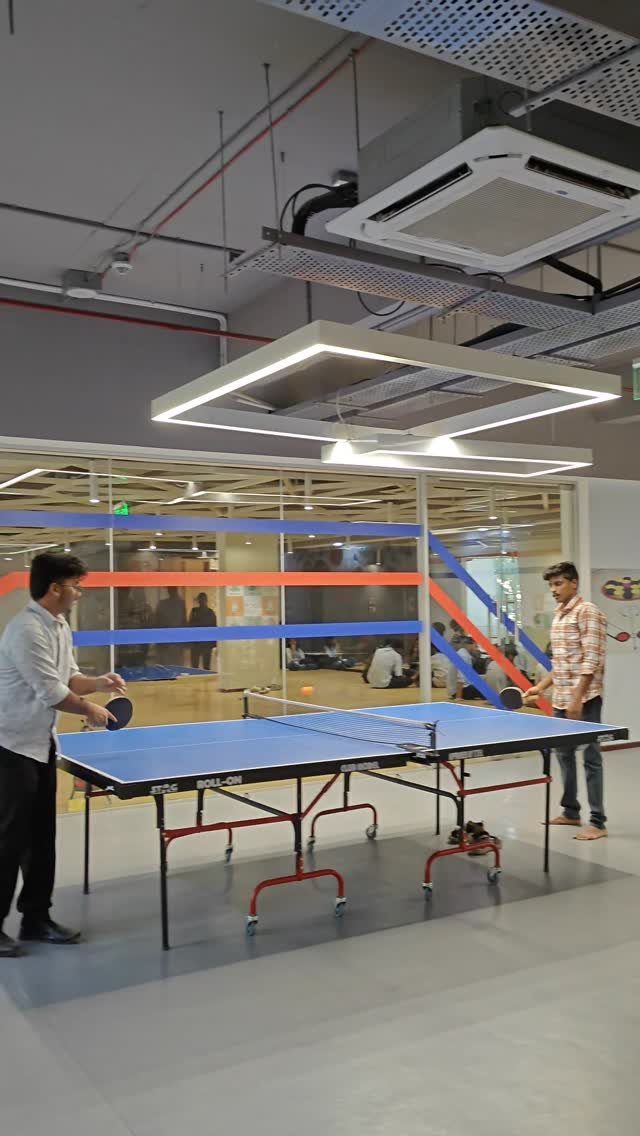 Two men playing table tennis on a blue table in a modern office.