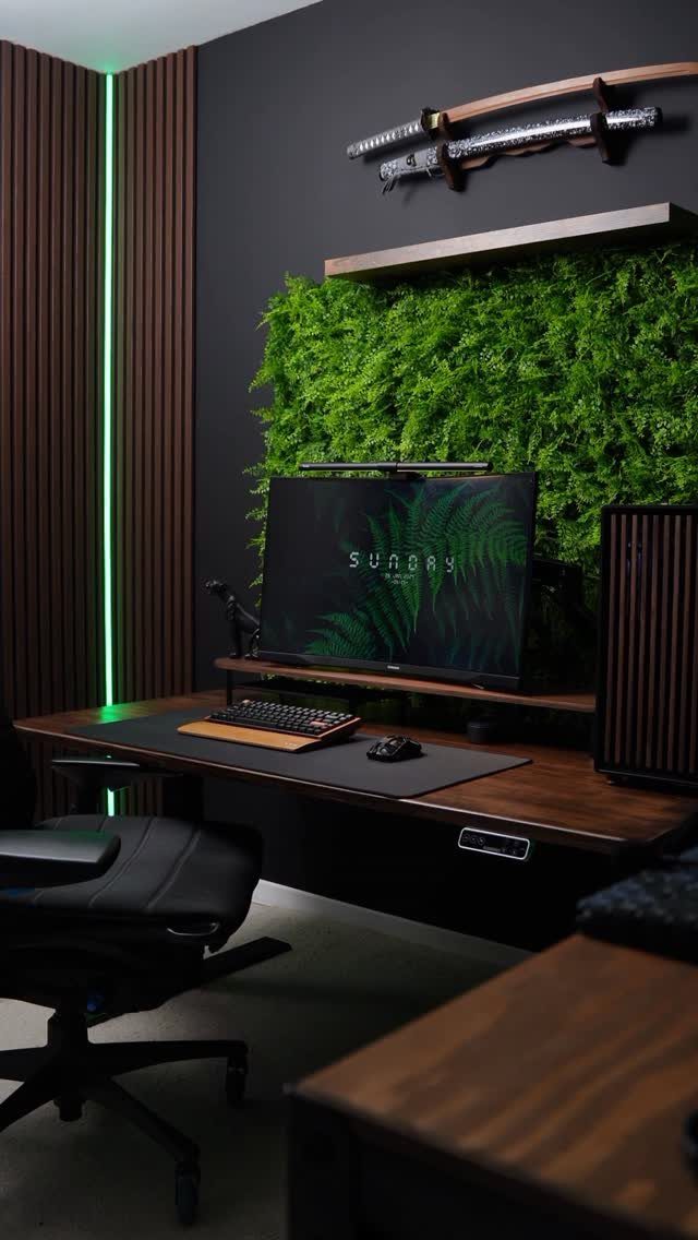 Gaming desk with a wooden surface, black chair, and a green plant wall.