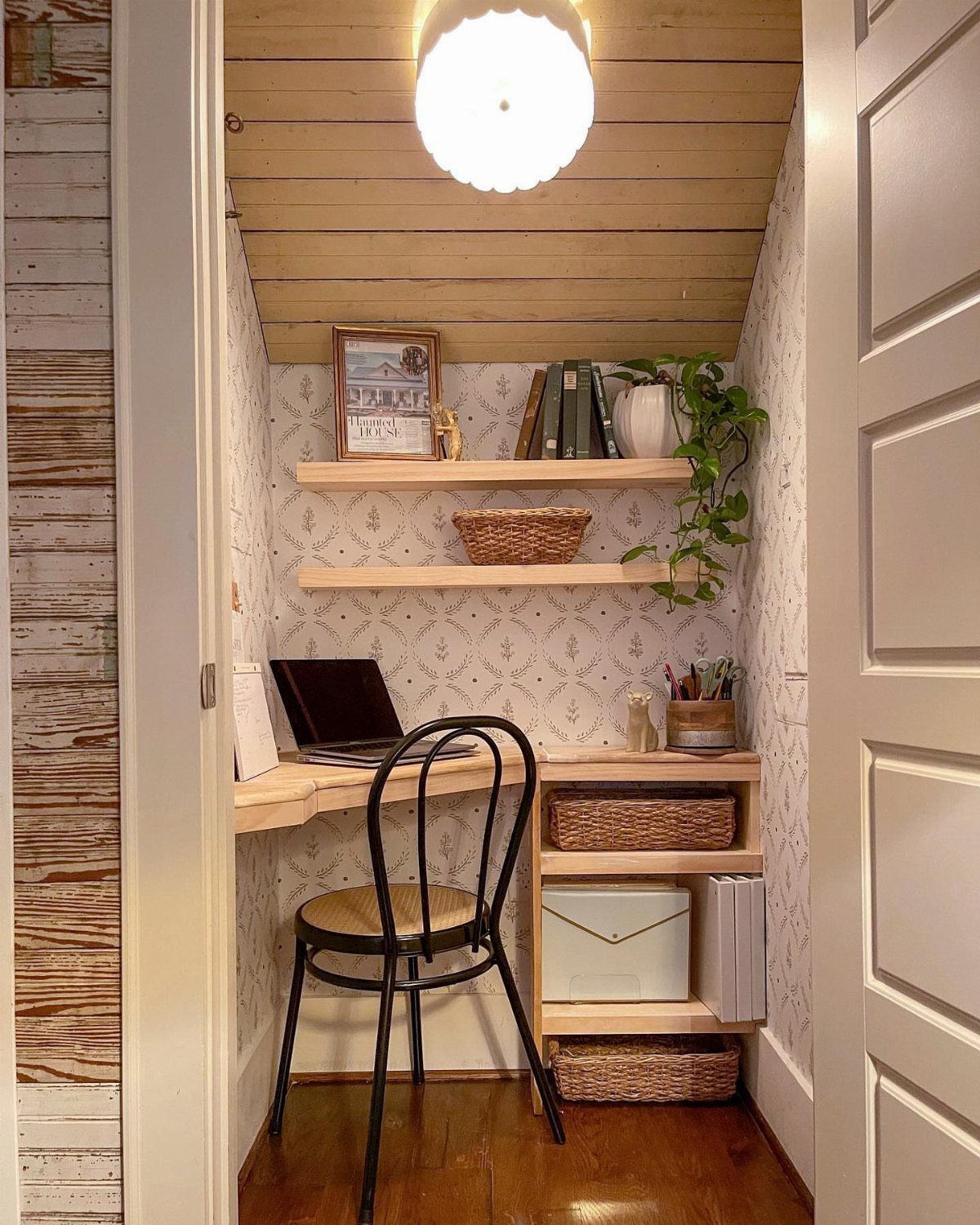 Closet office with a light wood desk, floating shelves, and a black chair.