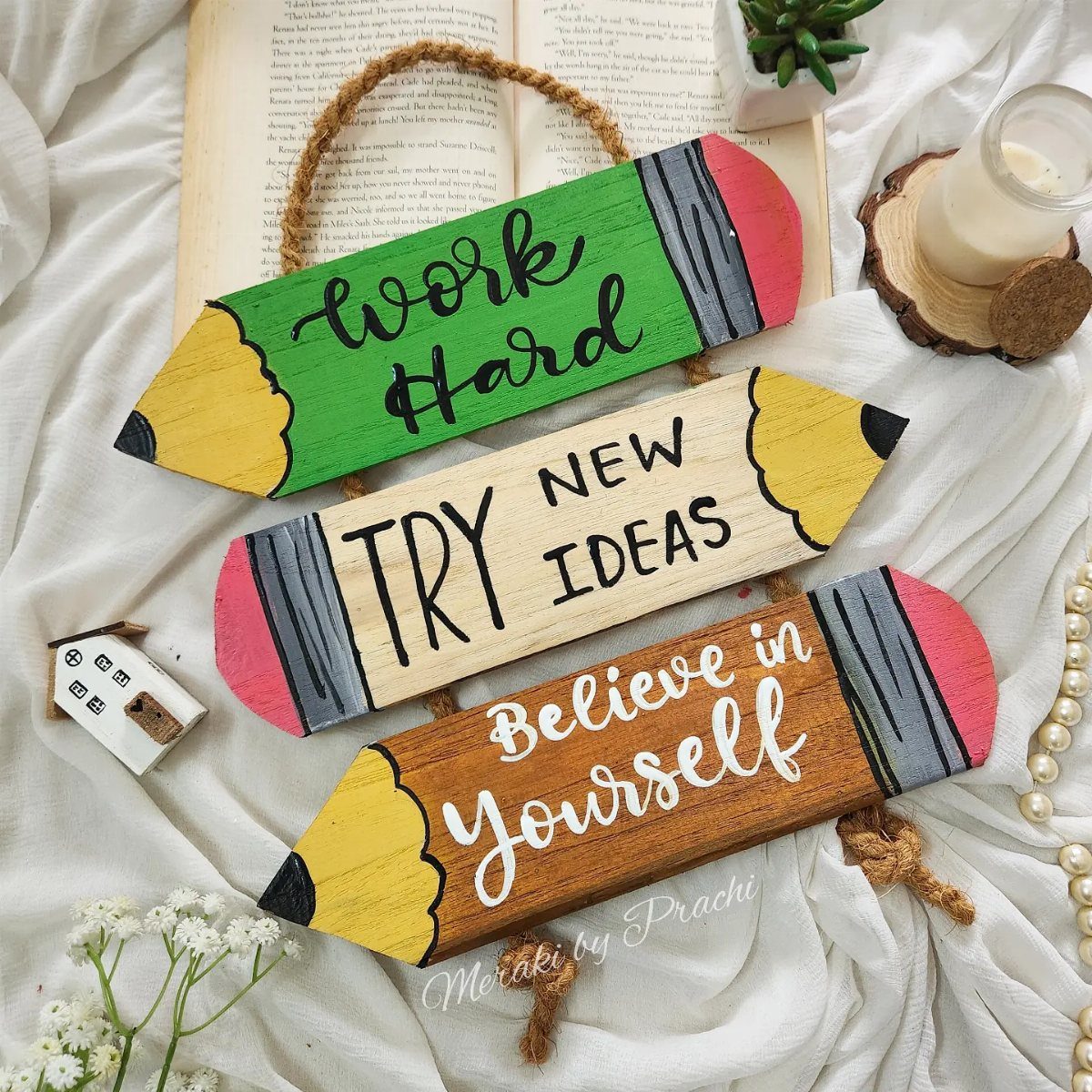 Three pencil-shaped wooden plaques with motivational quotes resting on white fabric.