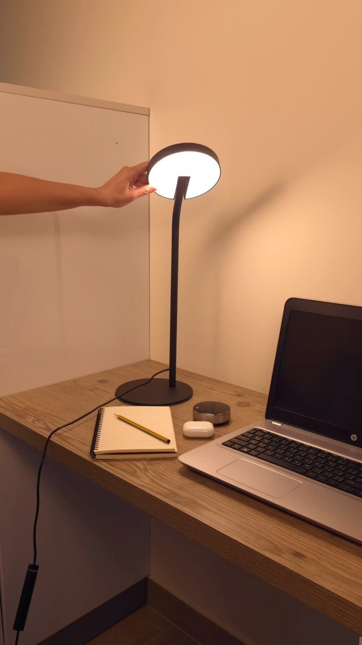 Modern black desk lamp illuminating a laptop and notebook on a wooden desk