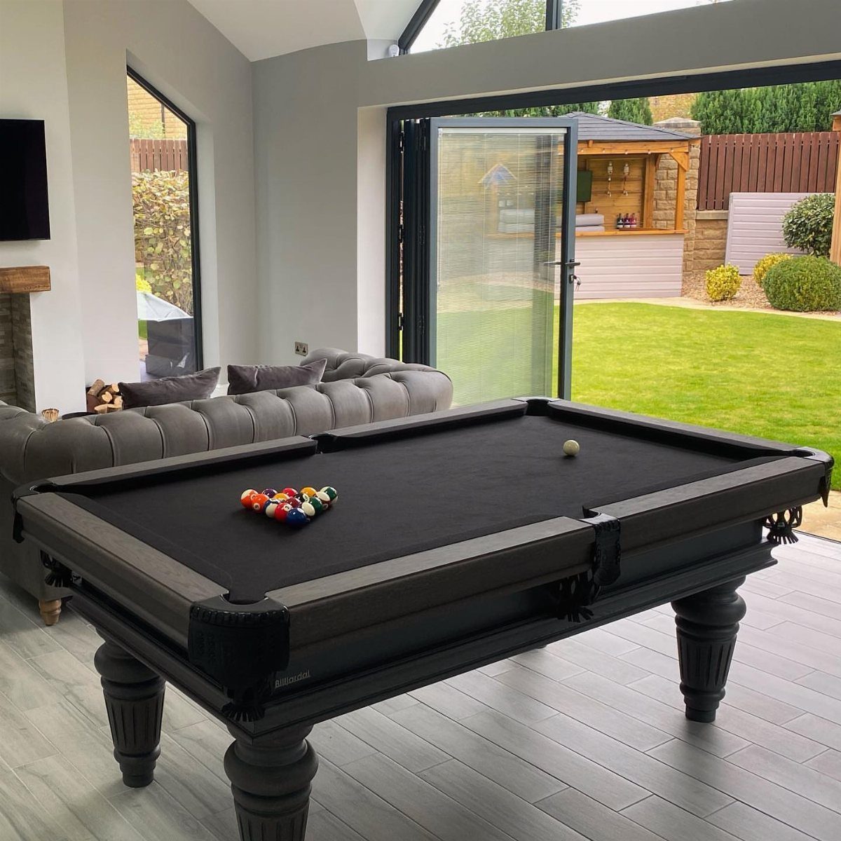 Black pool table with black felt in a modern room with grey sofa.