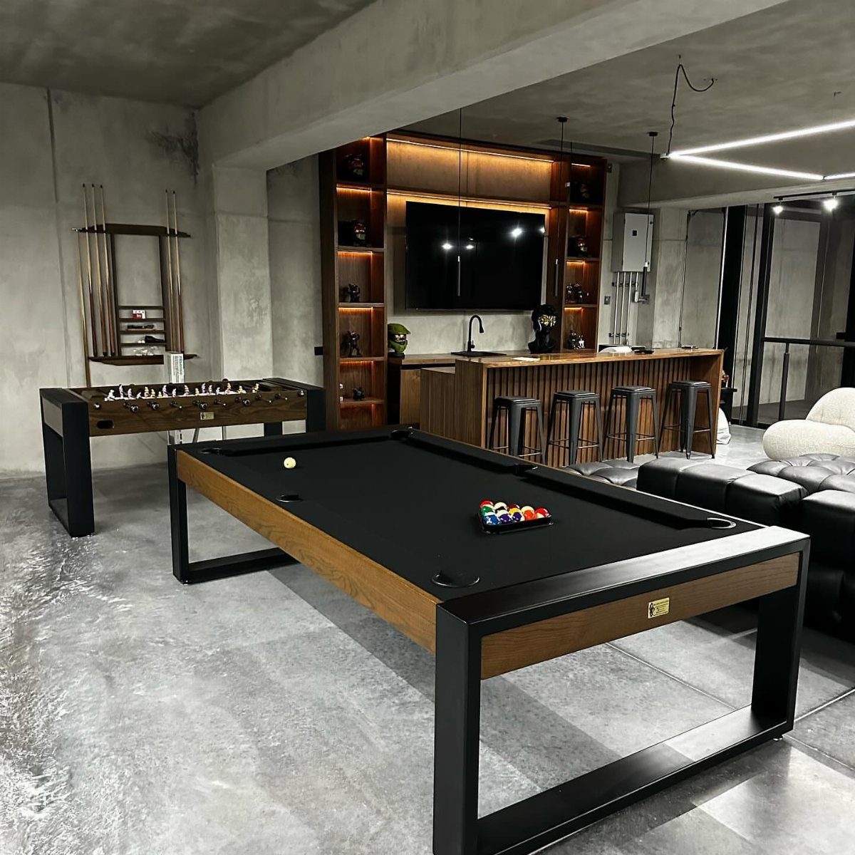 Modern game room featuring a pool table, foosball table, and black bar stools.