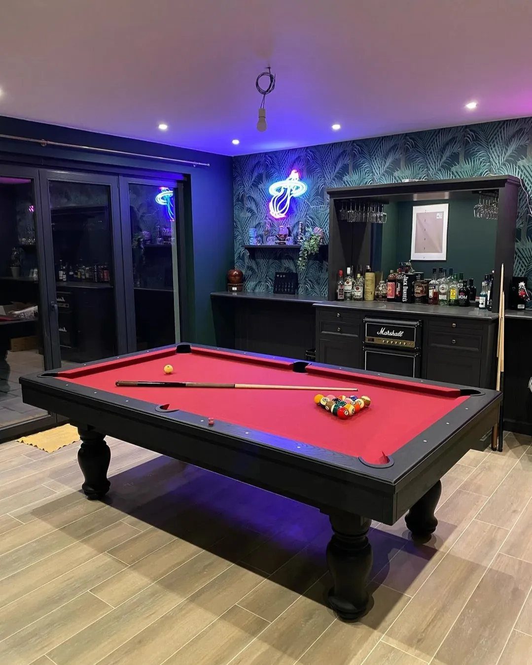 Black pool table with red felt in a room with teal wallpaper.