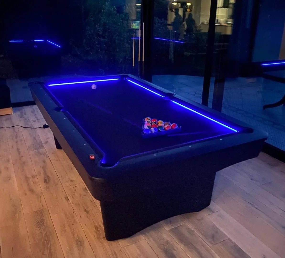 Modern black pool table with blue LED lighting on light wood flooring