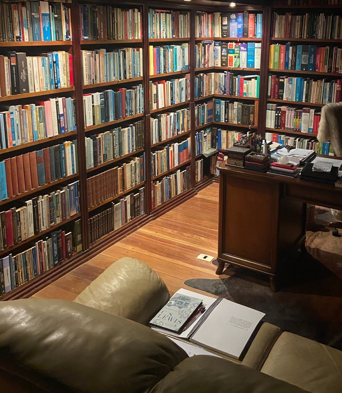 Wooden bookshelves filled with books surrounding a desk and tan leather sofa.