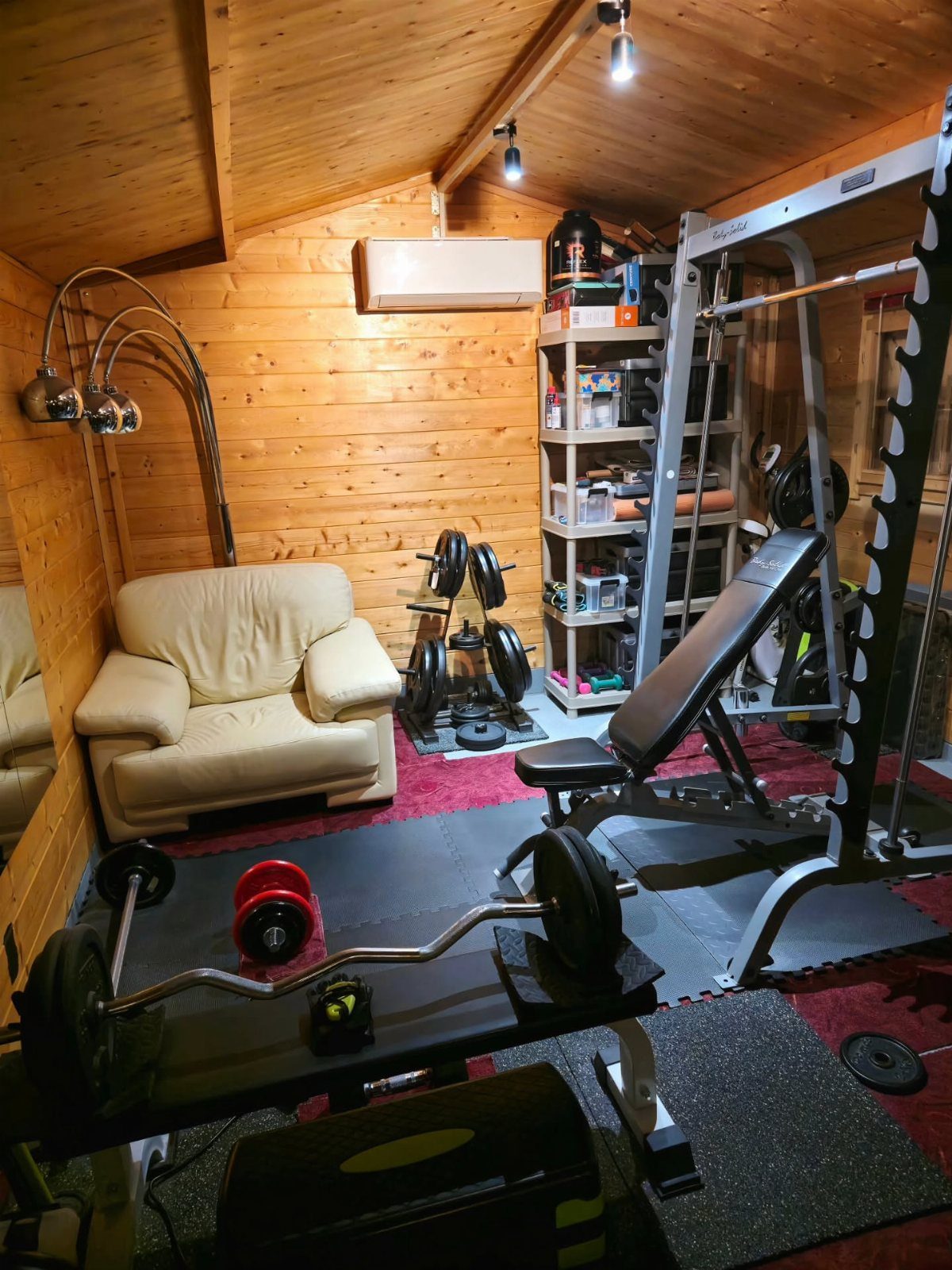 Home gym equipment including a weight bench and Smith machine in wood-paneled room.