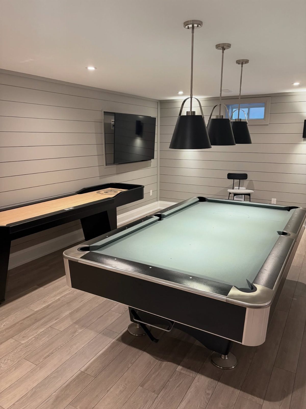 Modern recreation room featuring a blue pool table, shuffleboard, and black pendant lighting.
