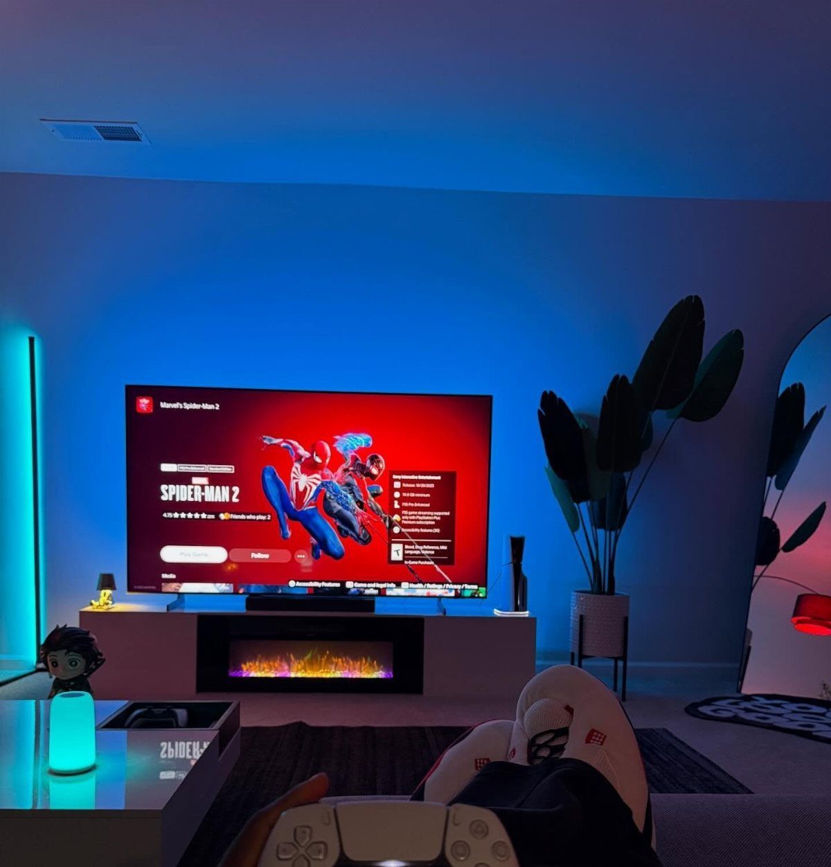 Modern gaming room with blue lighting, large TV, and electric fireplace console.