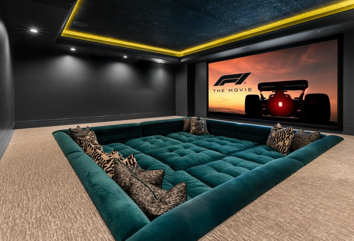 Teal velvet tufted pit sofa in a dark home cinema with large screen.