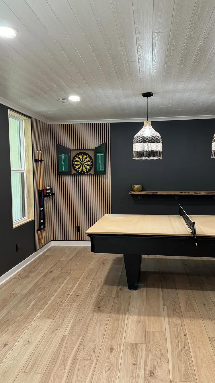 Ping pong table and dart board in a modern recreation room with wood flooring.