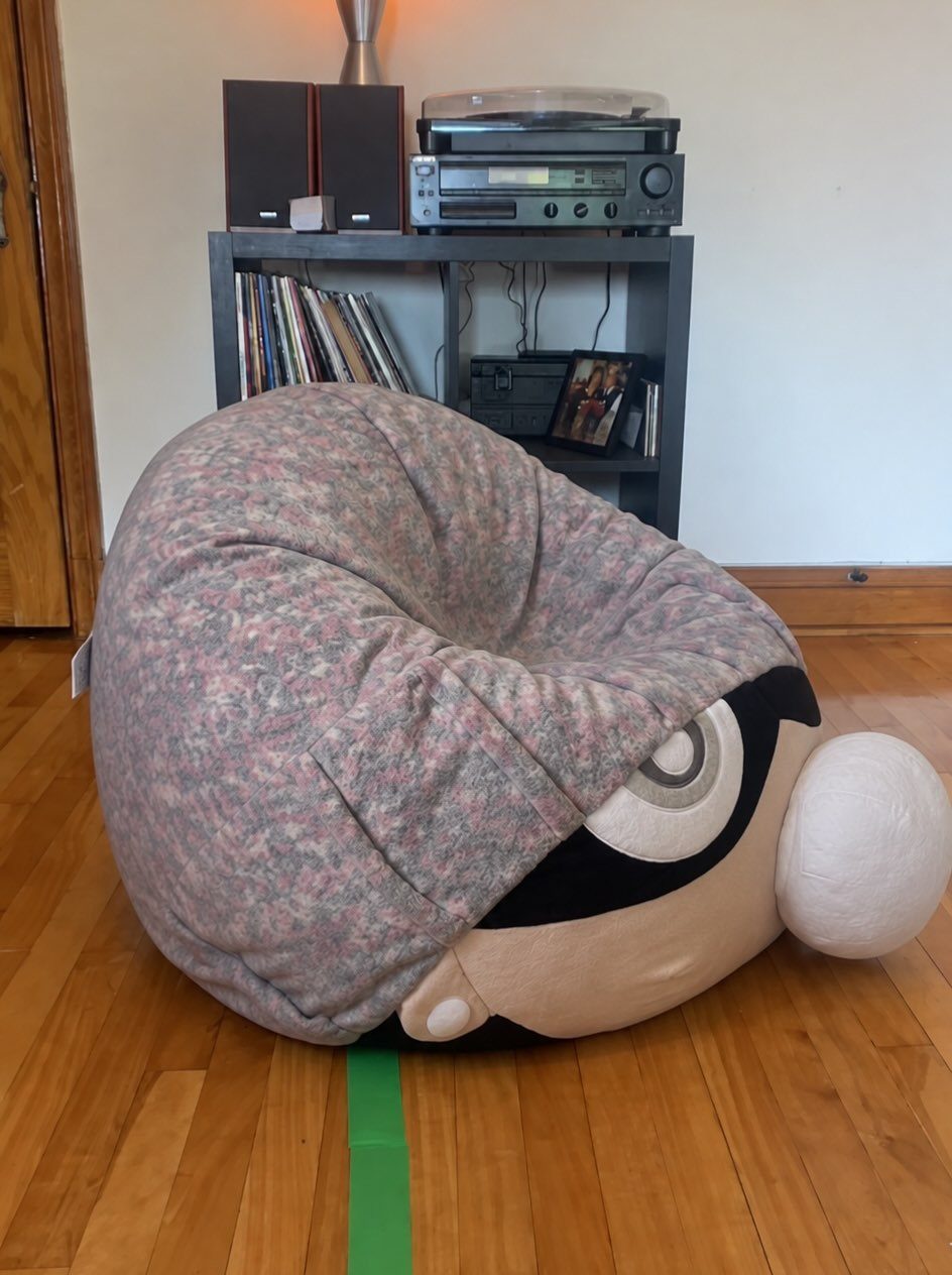 Character shaped bean bag chair on a wooden floor near a media shelf.