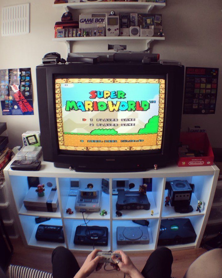 Retro gaming setup with a CRT television and consoles on white shelving units.