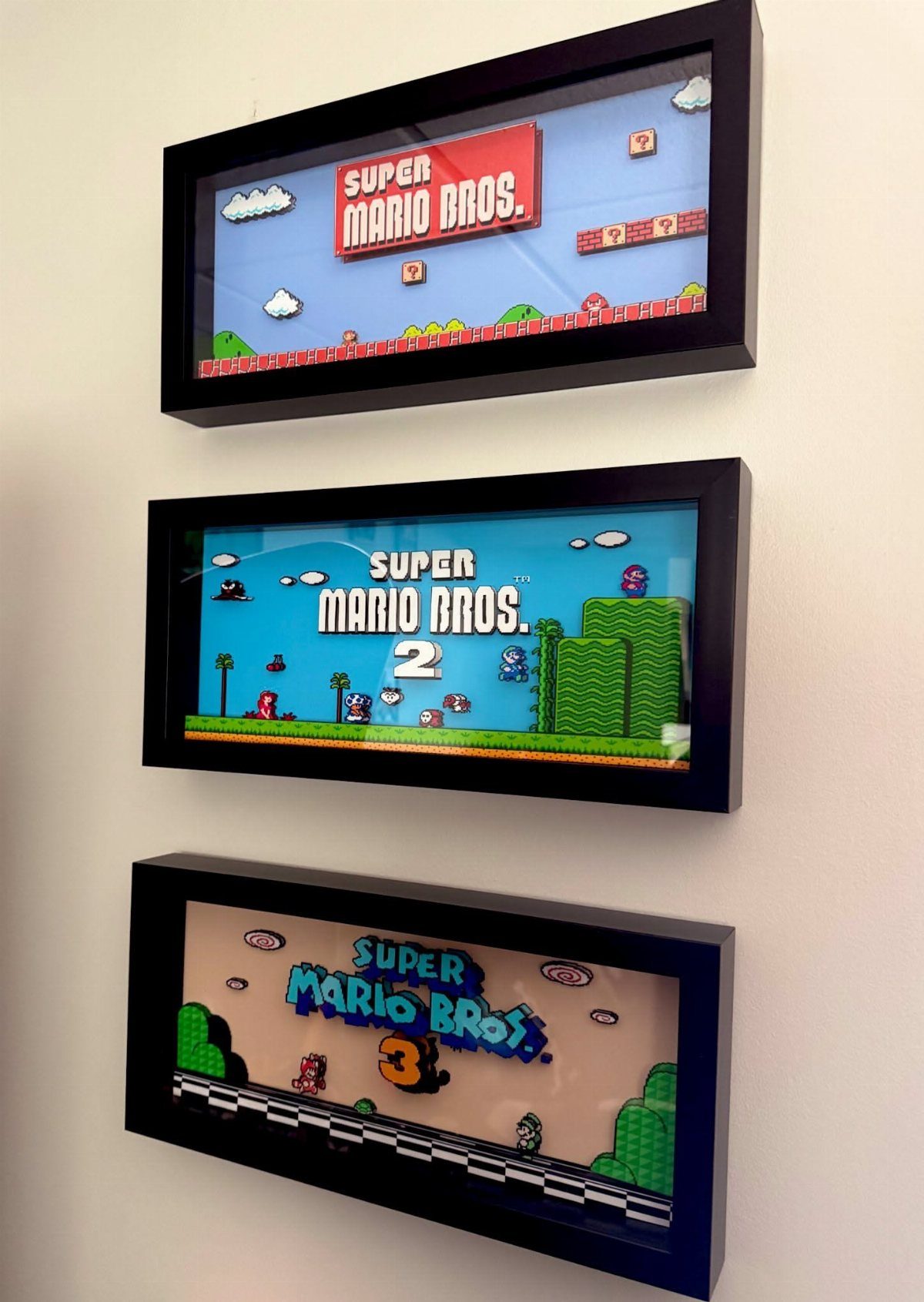 Three framed 3D pixel art scenes from Super Mario Bros on a white wall