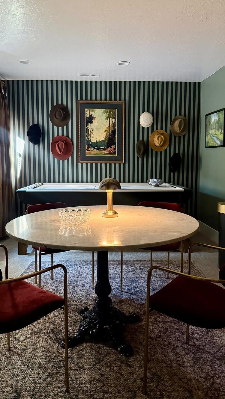 Round marble table with red velvet chairs against a green striped accent wall.