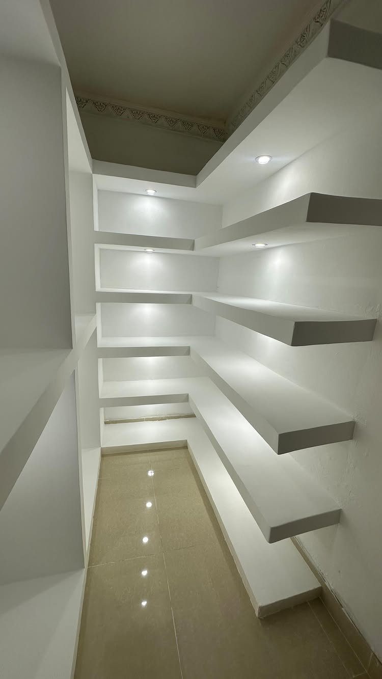 White built-in floating shelves with integrated spotlights in a modern room corner.
