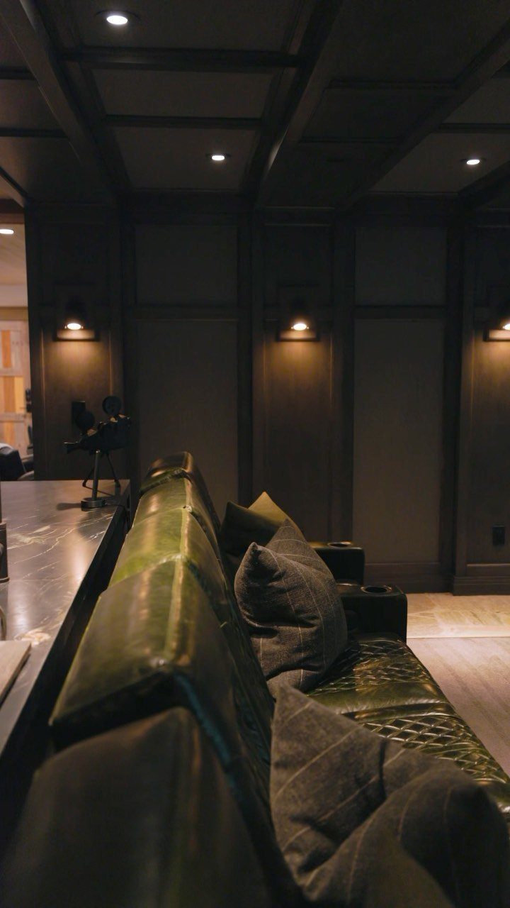 Green leather sofa in a dark wood paneled basement lounge with recessed lighting