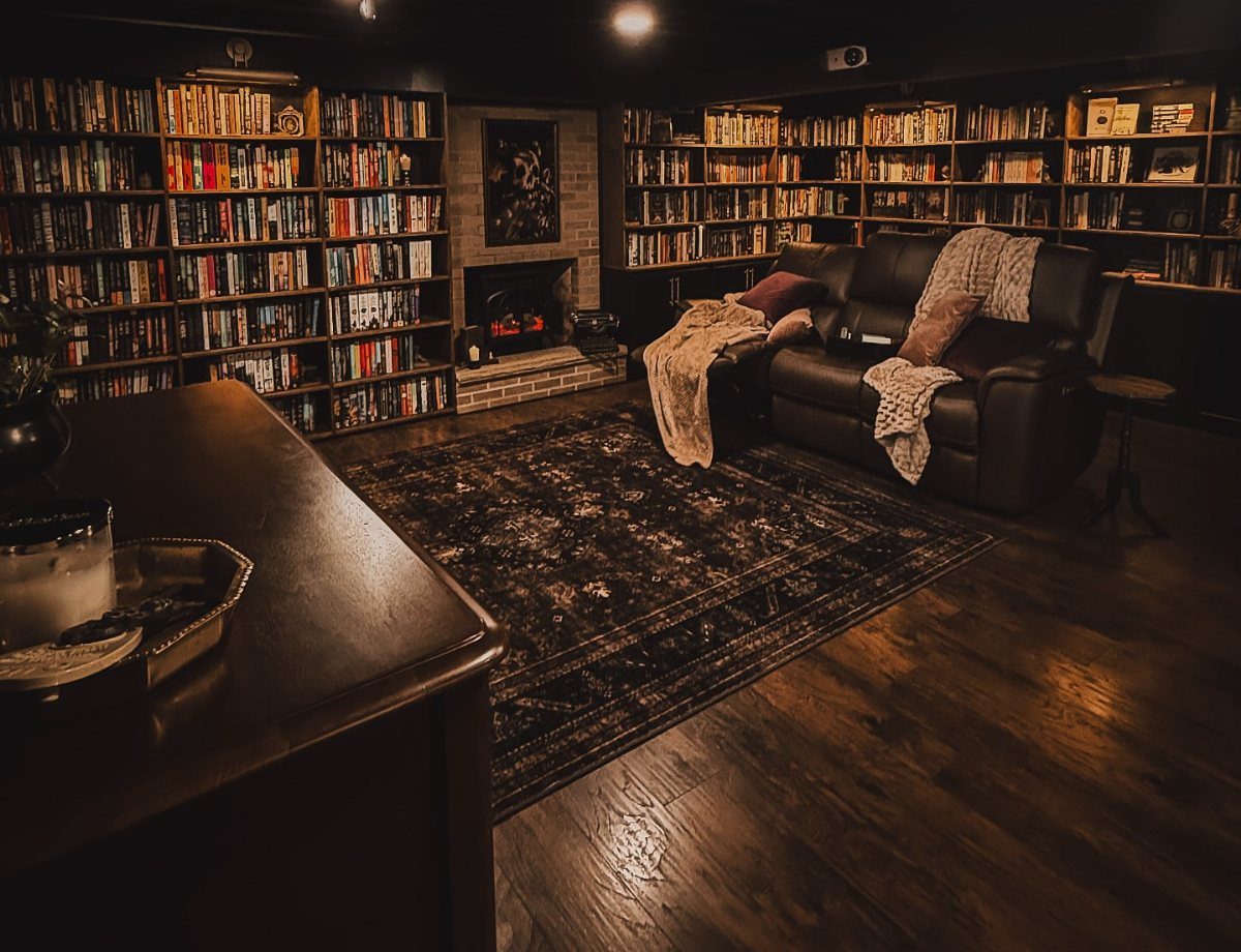 Cozy reading room with extensive bookshelves, leather sofa, and a small brick fireplace.