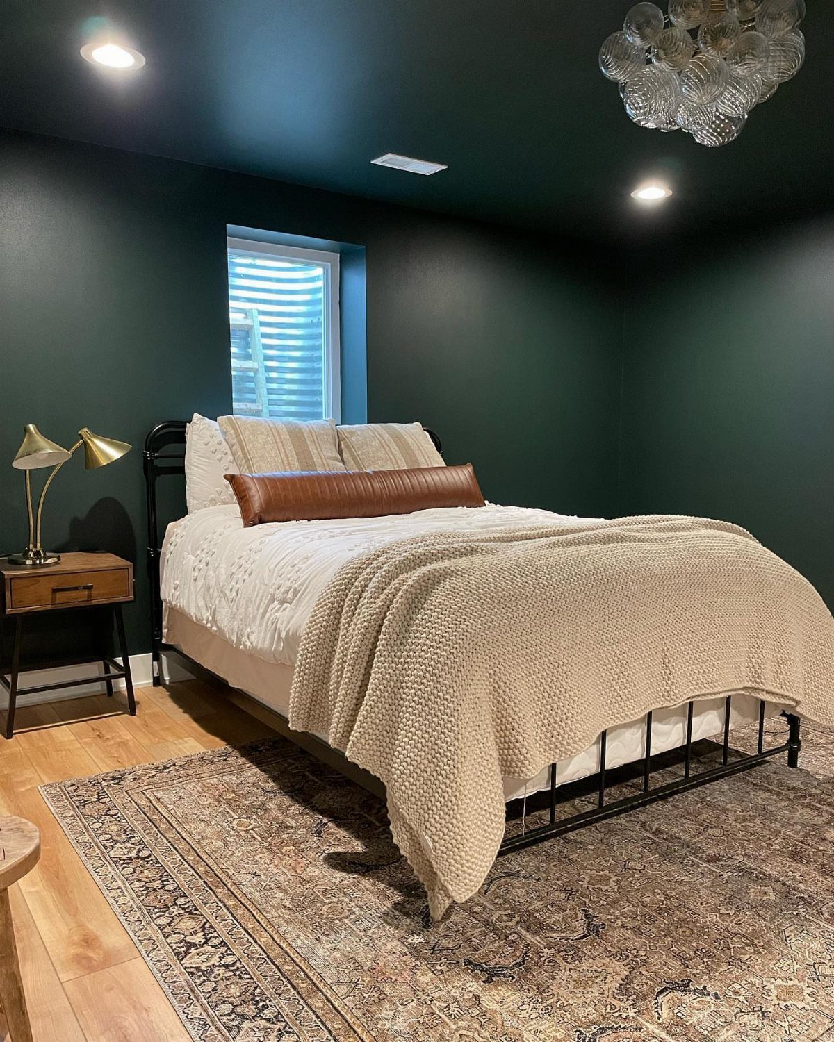 Bed with white linens and beige throw in a dark green bedroom