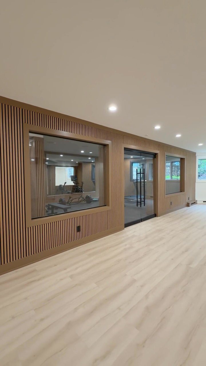 Modern basement hallway with wood slat walls and a glass-walled home gym room.