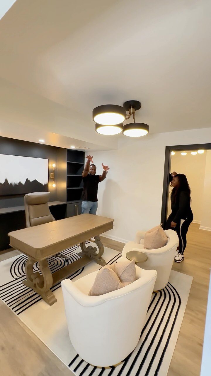 Modern home office with wooden desk, white armchairs, and striped area rug.