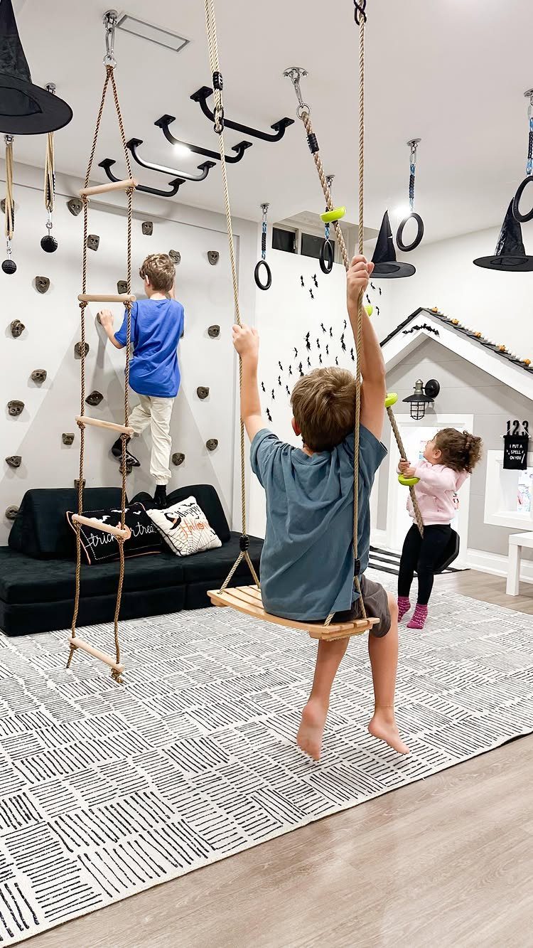 Children playing on a climbing wall and swing in a modern basement playroom.