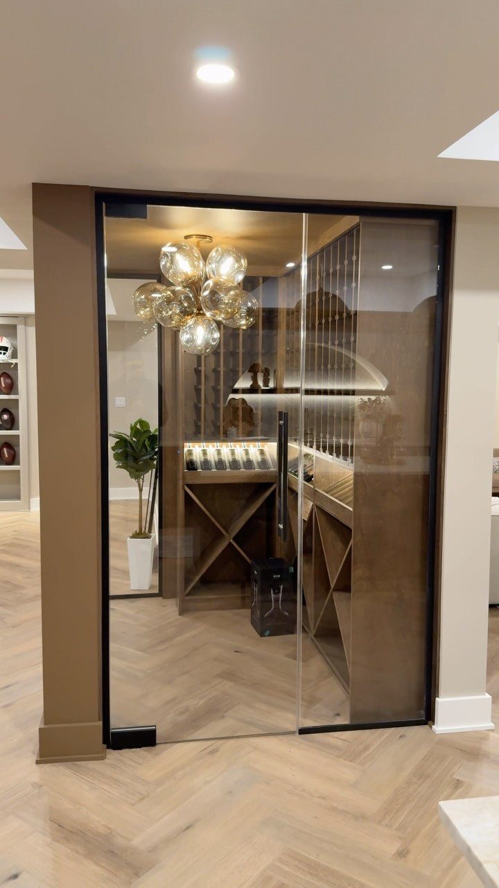 Glass-enclosed wine cellar with wooden racks, tasting counter, and bubble chandelier.
