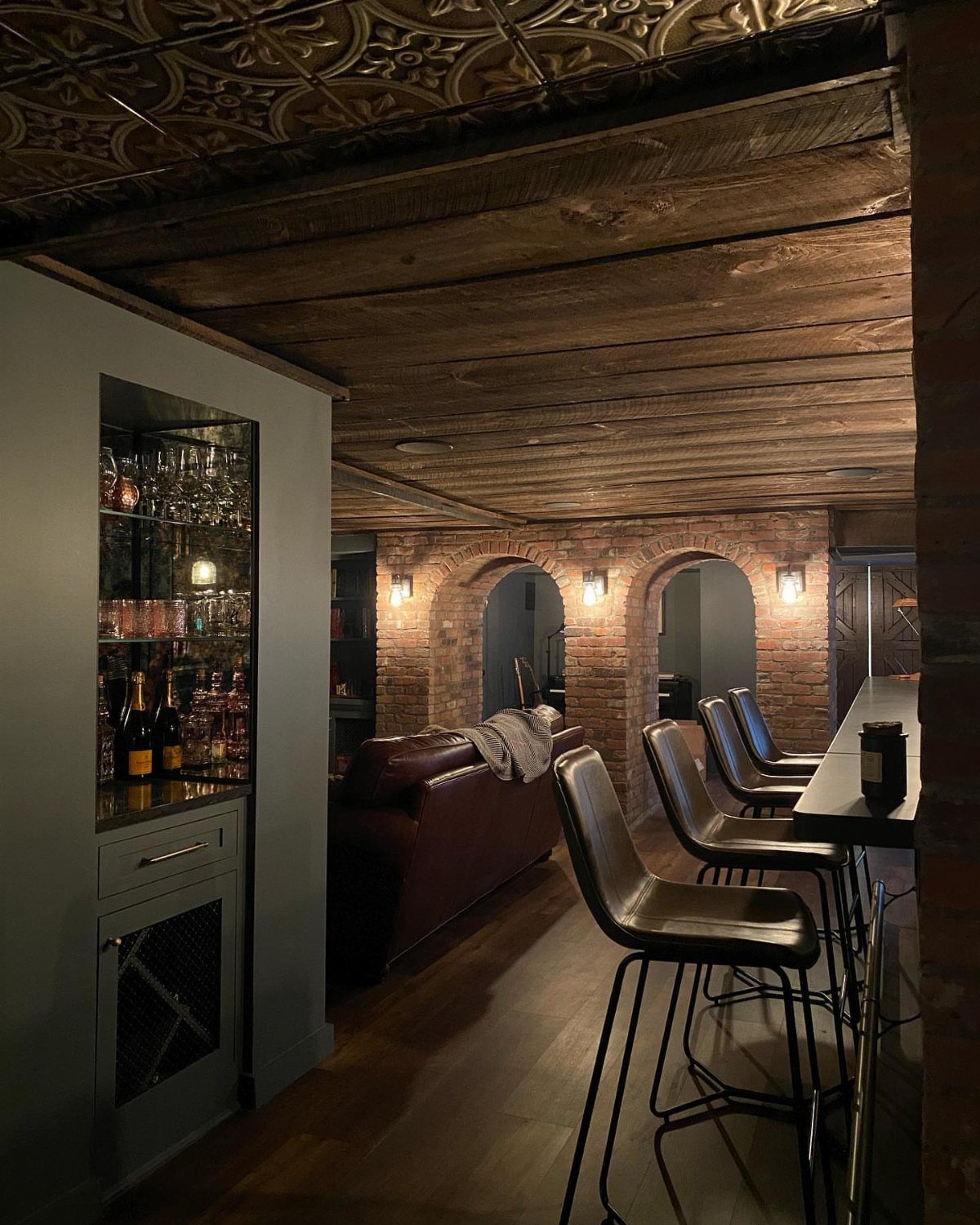 Basement lounge with a built-in bar, leather sofa, and exposed brick walls.