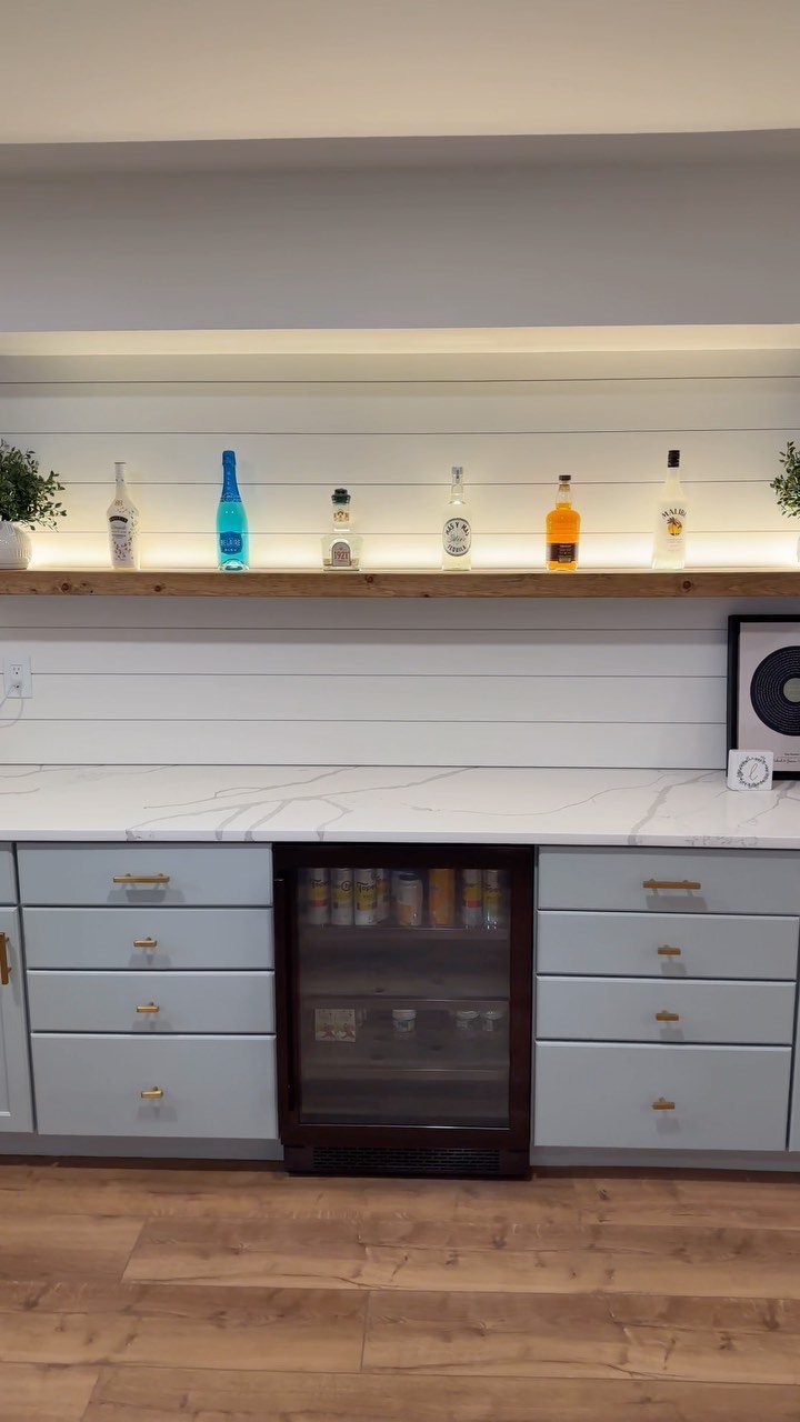 Small farmhouse style basement bar with white shiplap walls and wooden floating shelf.