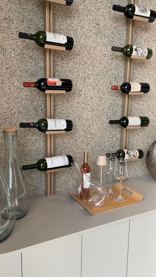 Vertical wooden wine racks holding bottles on a speckled wall above a countertop.