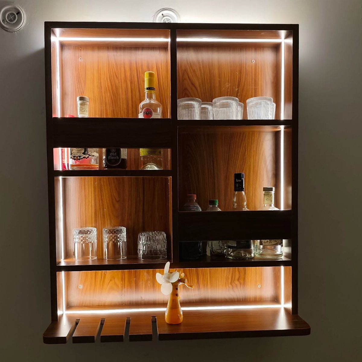 Wall-mounted wooden bar unit with LED lighting, liquor bottles, and glassware.