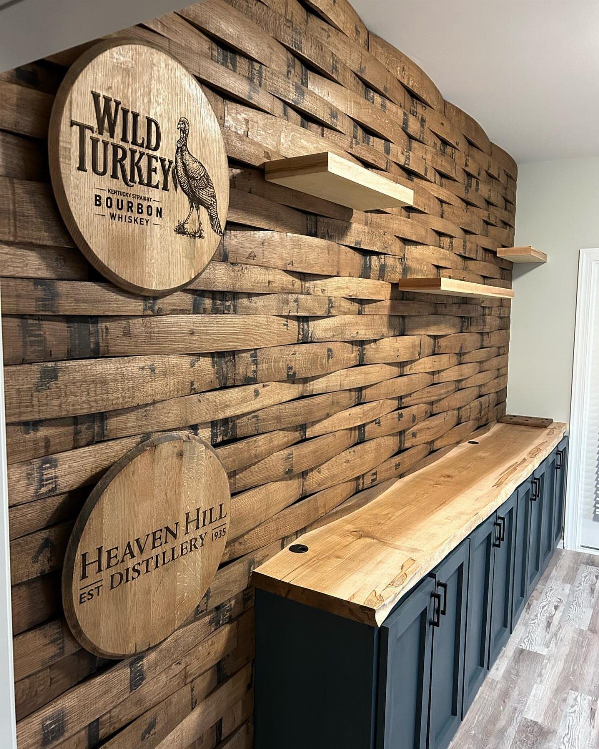 Rustic home bar with live-edge wood top, dark cabinets, and barrel slat wall.