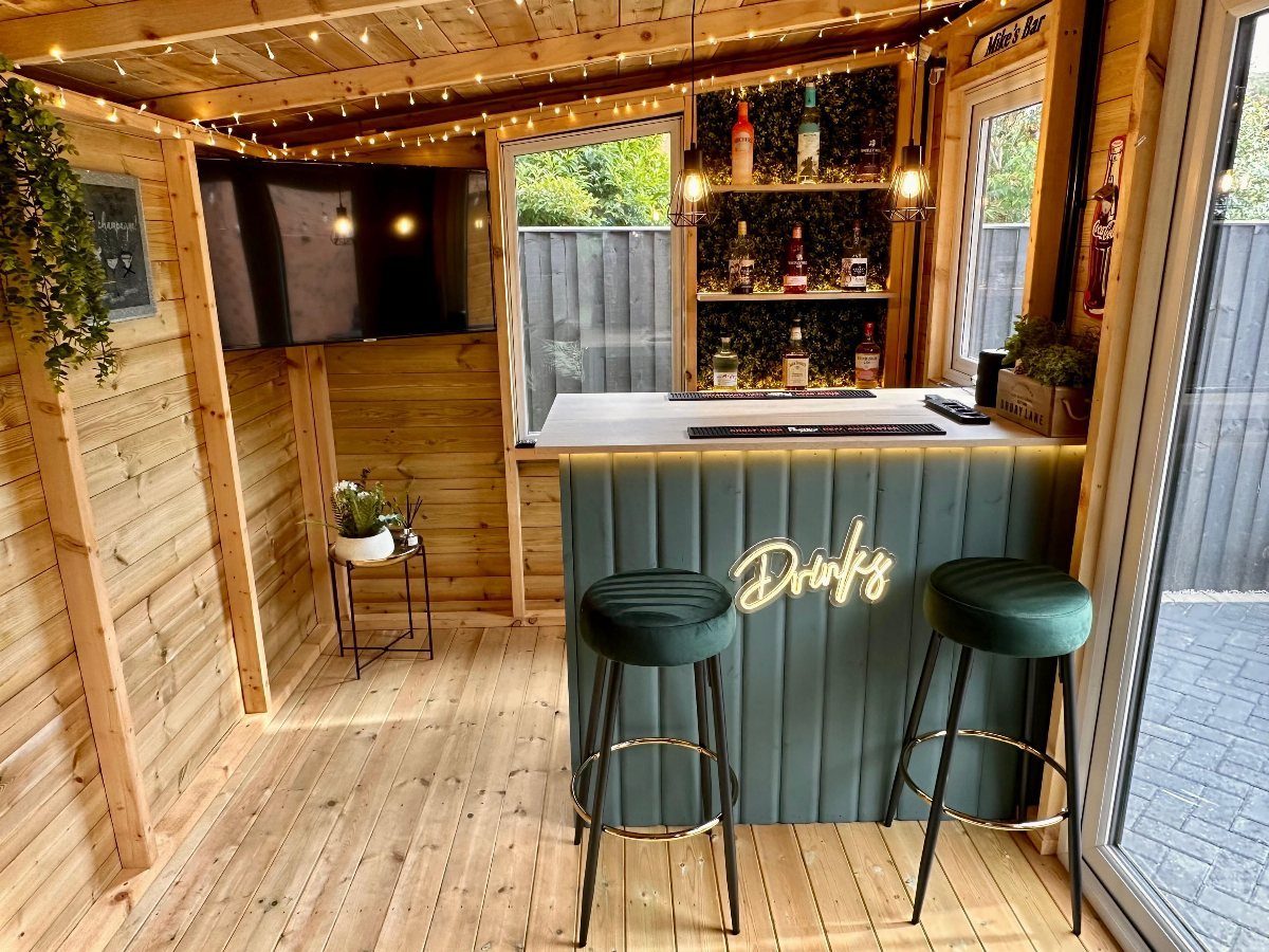 Teal home bar with white countertop and green velvet stools in wooden room