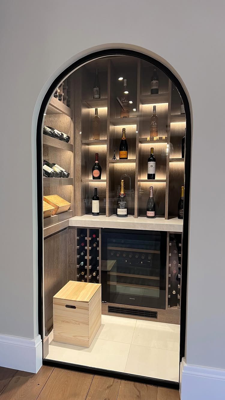 Arched built-in home bar with light wood shelving, wine refrigerator, and bottle storage.