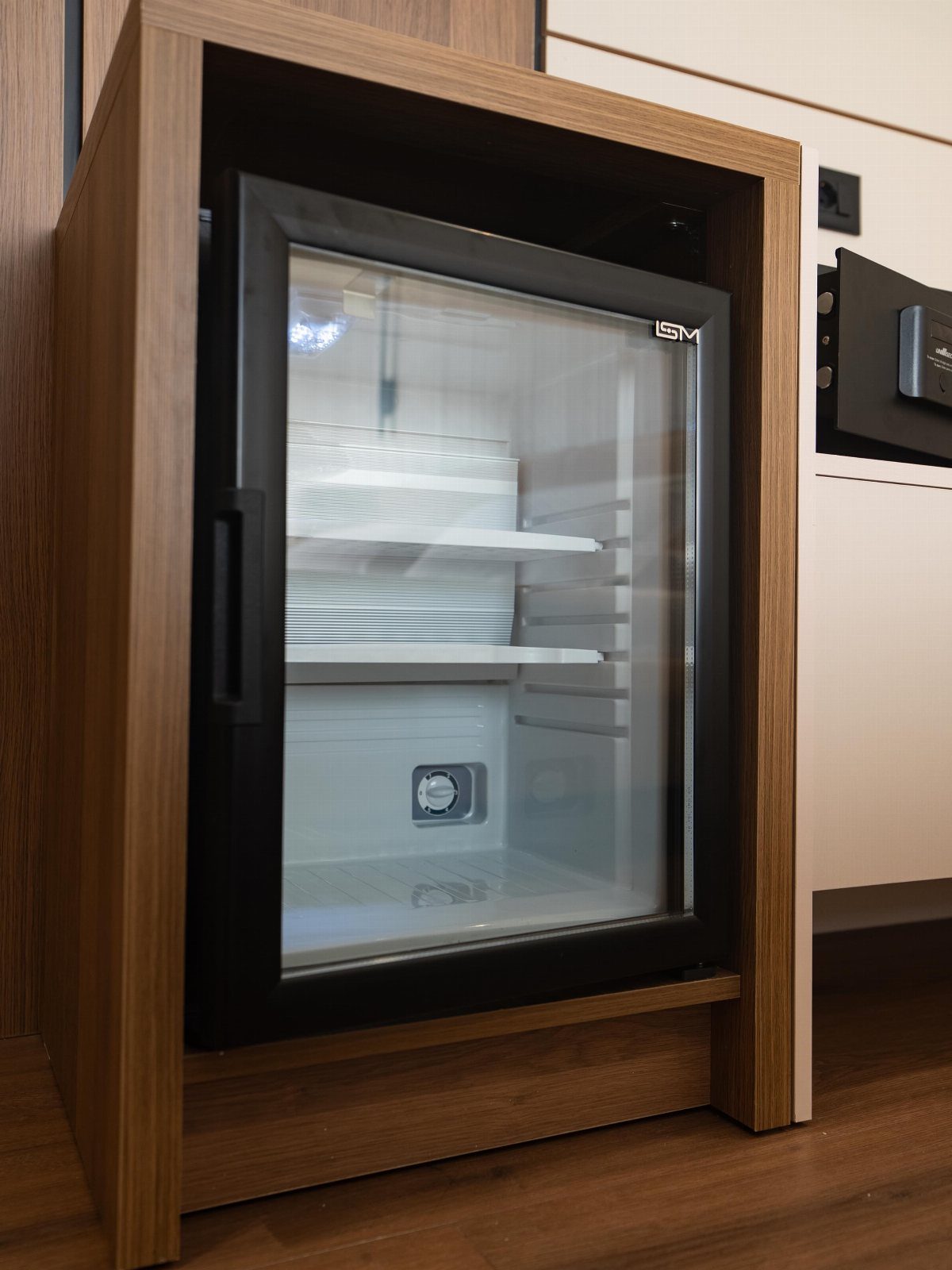 Mini refrigerator with glass door built into a light brown wooden cabinet frame.
