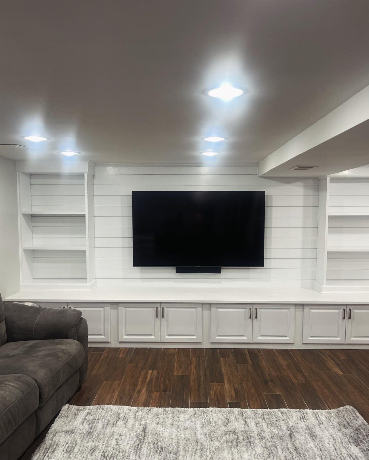 White built-in shelving and cabinets surrounding a television in a modern basement room.