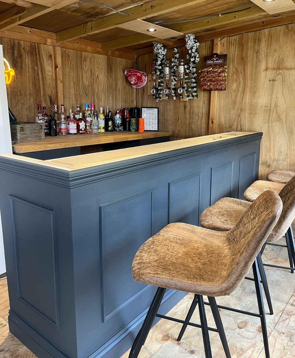 Grey paneled bar counter with brown textured stools against wood-paneled walls.