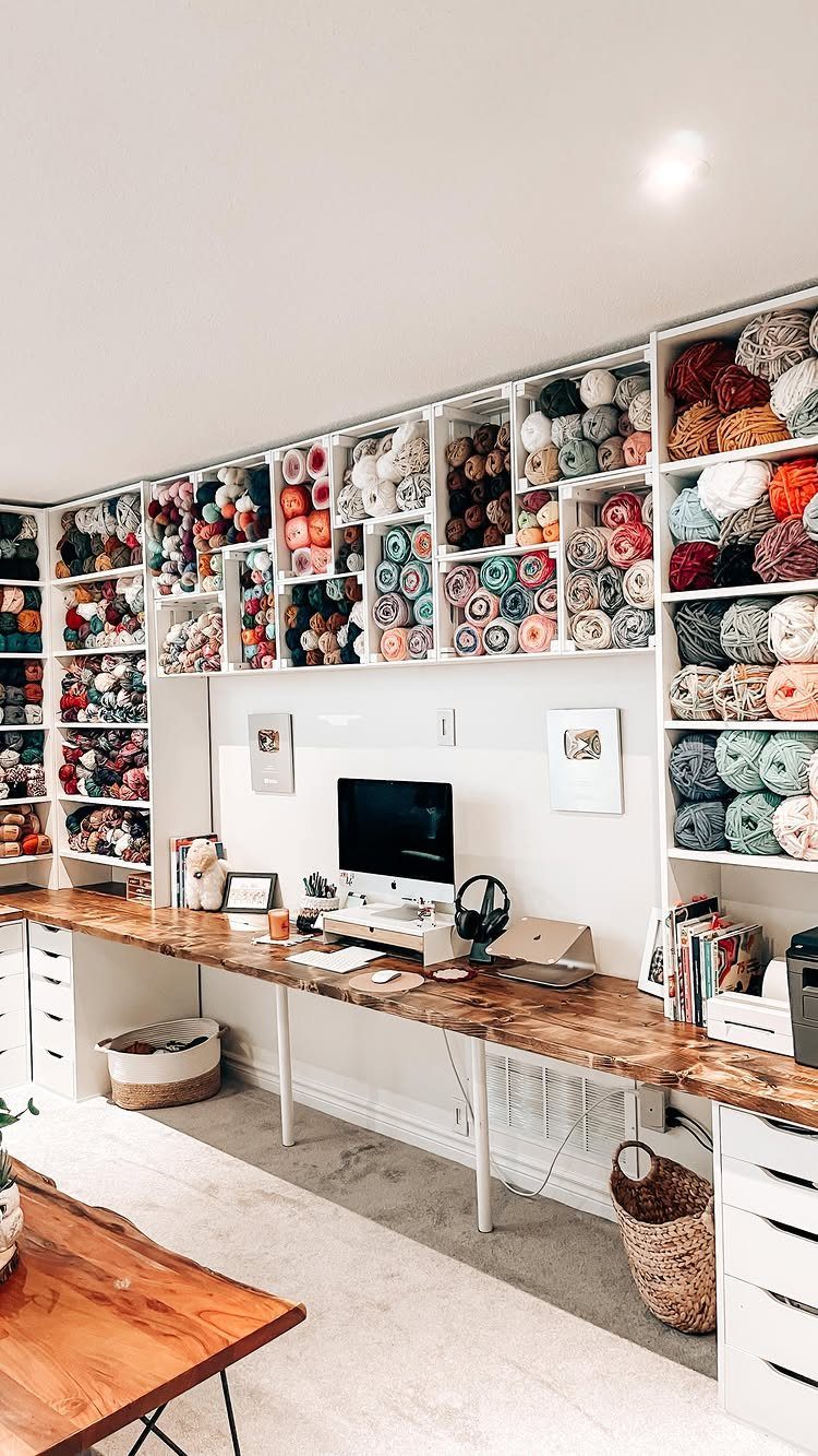 Wooden craft desk with a computer and shelves filled with colorful yarn.