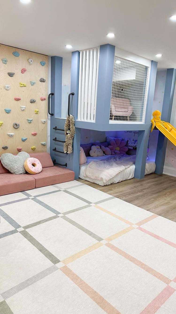 Children's playroom with a blue loft bed, yellow slide, and colorful climbing wall.