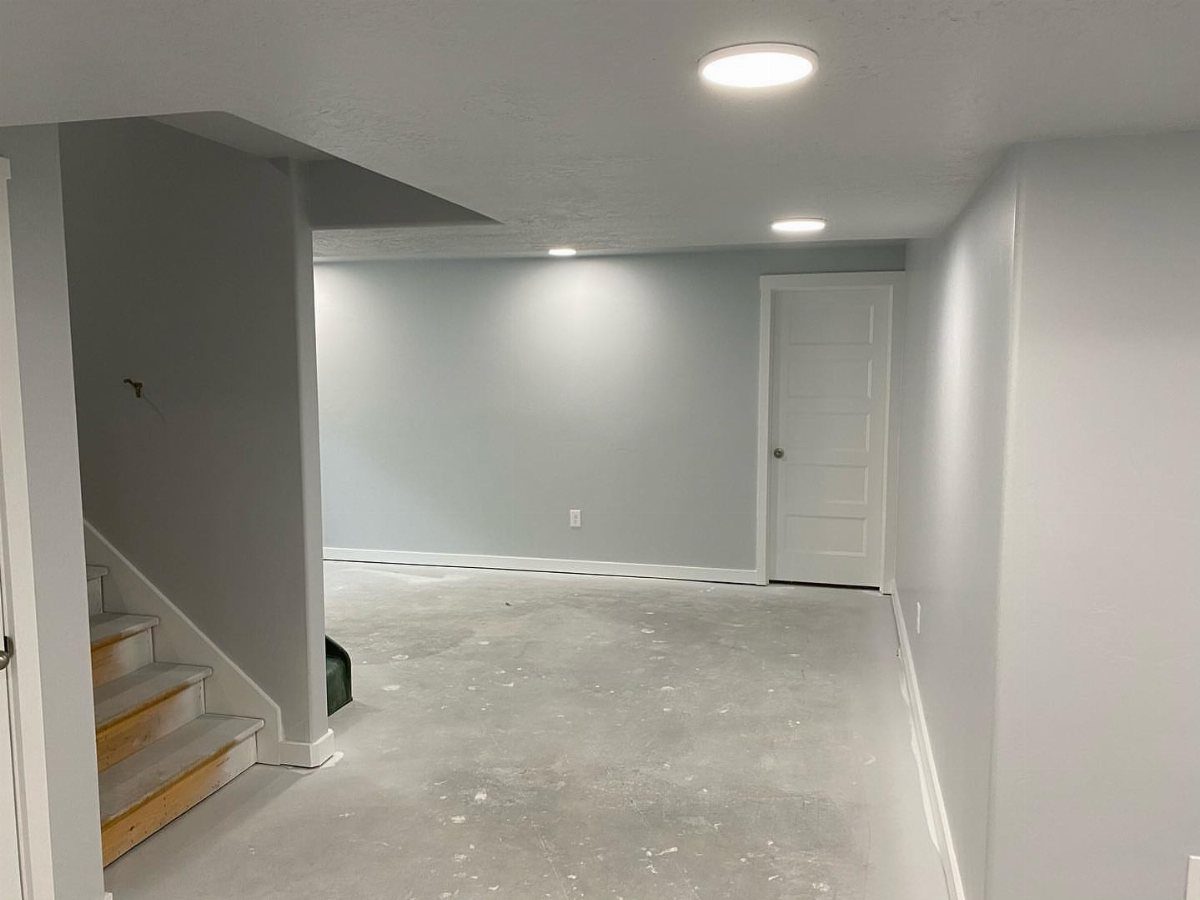 Empty basement room with light grey walls, white trim, and recessed ceiling lights.