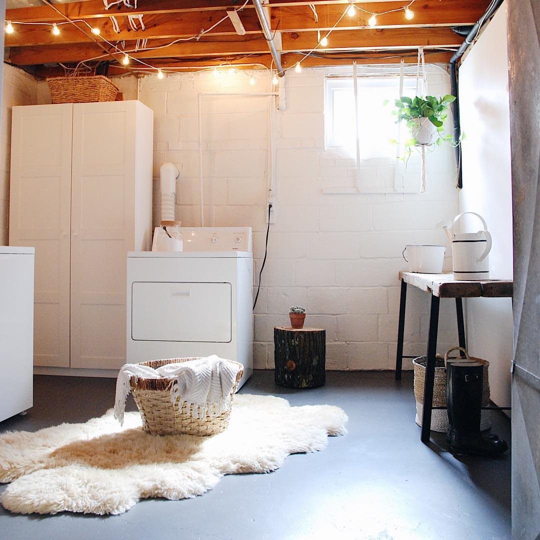 White laundry room in a basement with exposed beams and string lights.