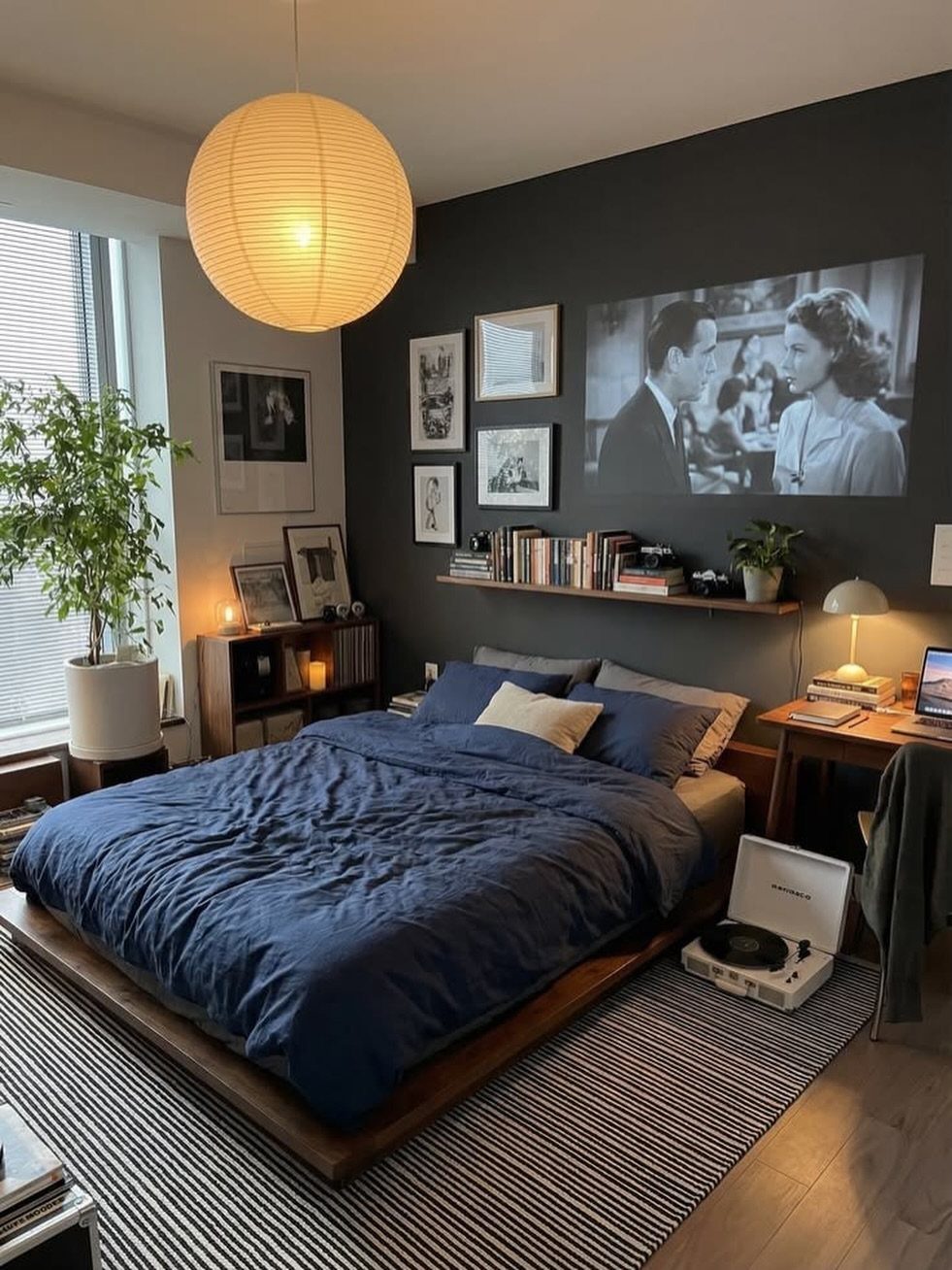 Bedroom with dark charcoal grey accent wall, navy blue bedding, and warm lighting.