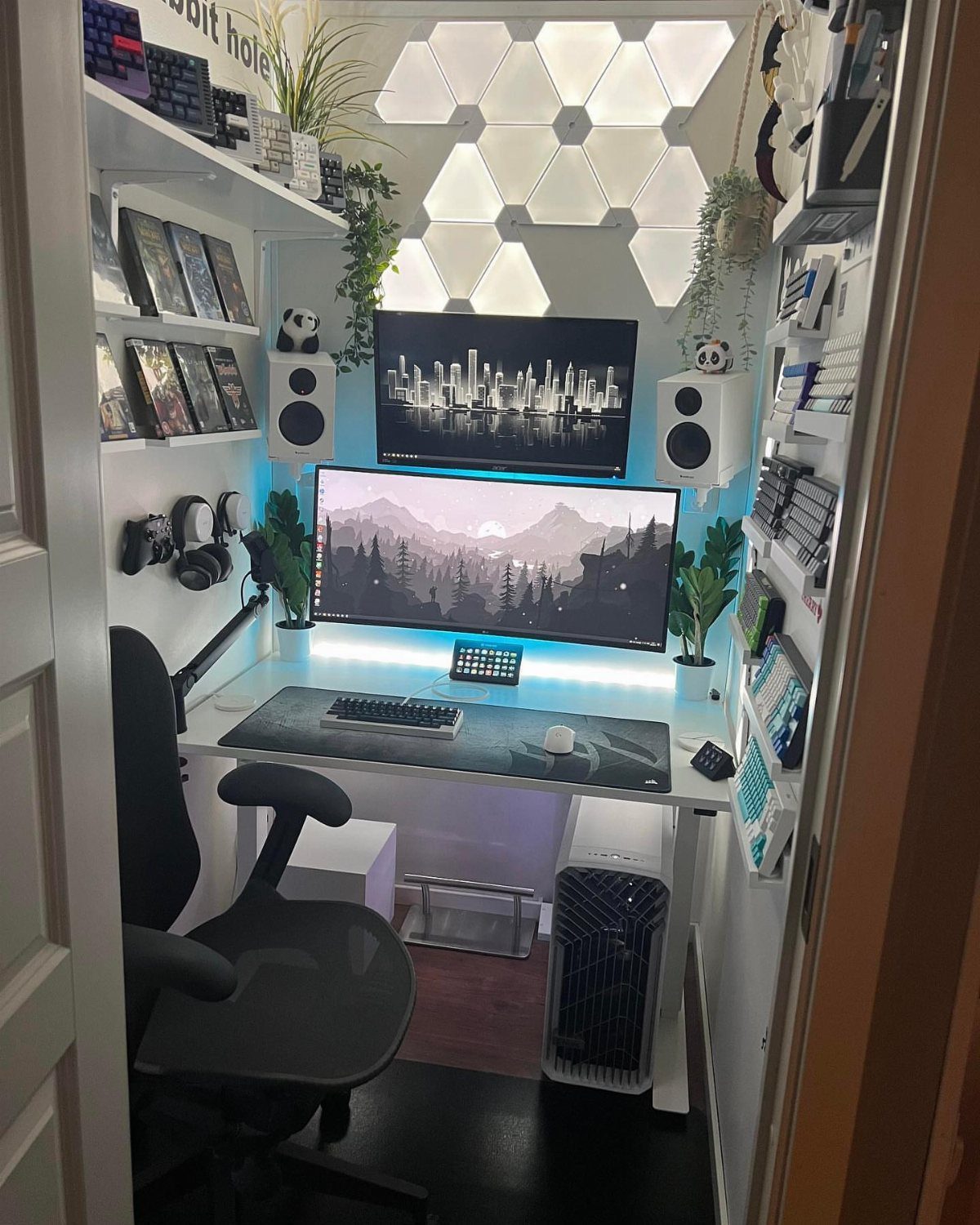 Gaming setup with dual monitors, hexagonal wall lights, and a black ergonomic chair.