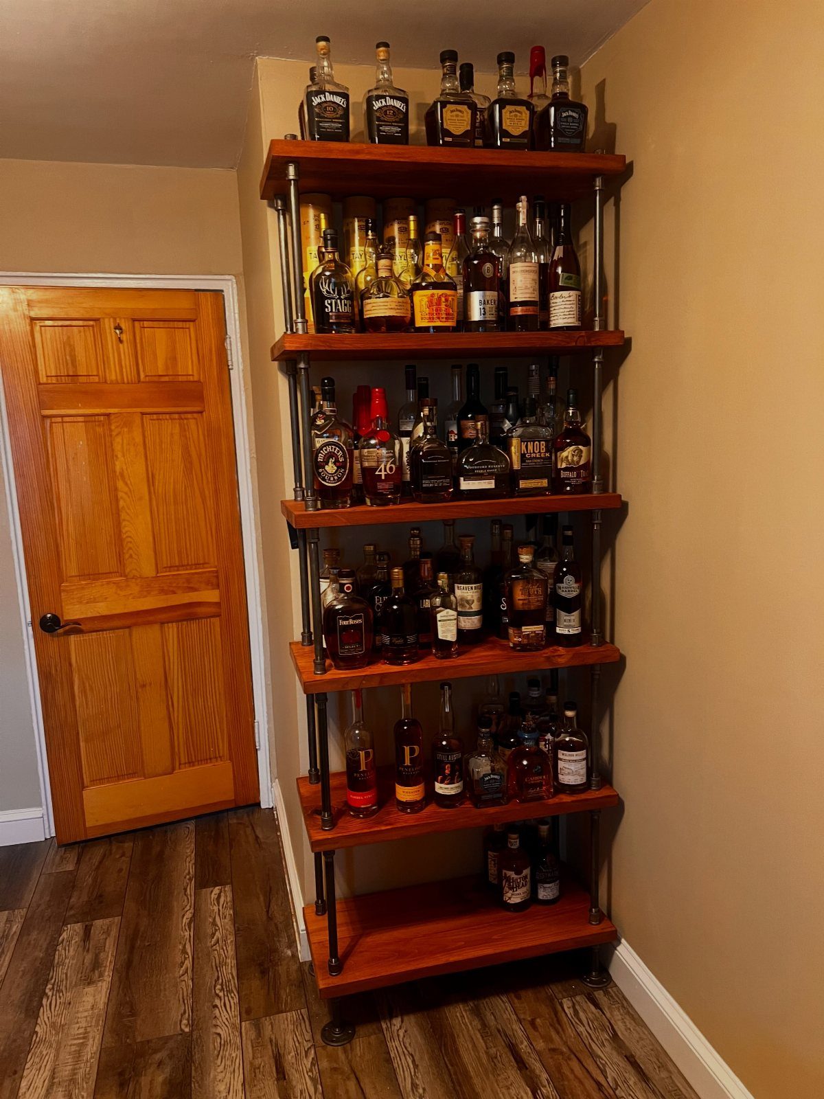 Industrial wooden liquor shelf filled with bottles next to a wooden door.