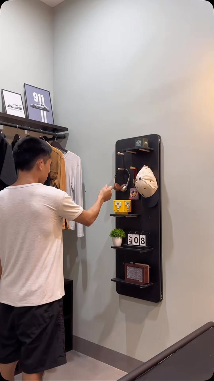 Man organizing items on a black wall-mounted pegboard in a modern room.